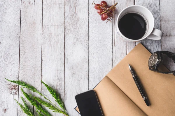Beyaz ahşap masa arka plan üzerinde boş defter, kalem, üzüm, saat, akıllı telefon ve çeltik pirinç ile Kahve fincan üst görünümü, metin için boş alan