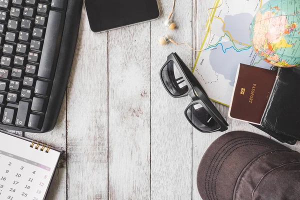 白い木製テーブルの背景、旅行の概念にカレンダー、スマート フォン、イヤフォン、サングラス、キャップ、財布、パスポート、地図、世界中にキーボードの上から見る — ストック写真