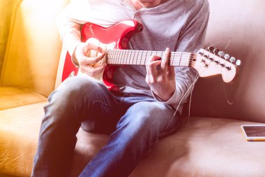 Casual genç adam evde kanepede gitar çalmak.