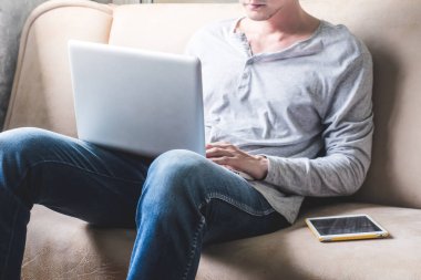 Kanepe evde tablet ile dizüstü bilgisayar kullanarak rahat genç adam.