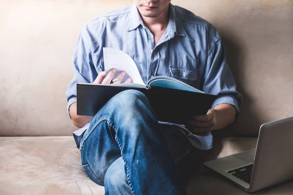 Casual young man reading documents on sofa at home.