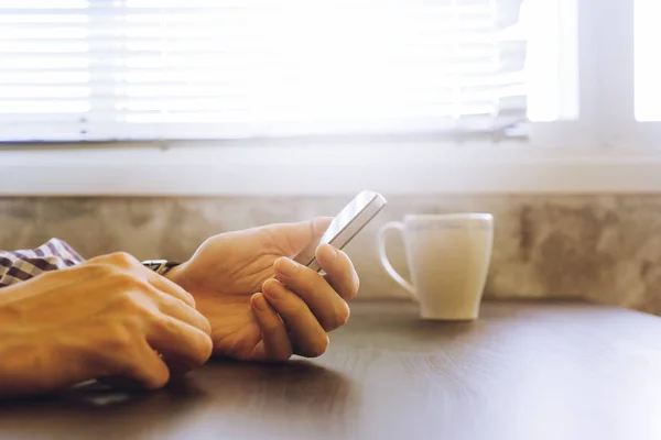 Primer plano de las manos masculinas usando un teléfono inteligente en el escritorio, tonificado con luz solar . — Foto de Stock