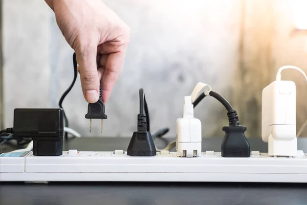 Hand hält elektrischen Stecker, Mehrfachsteckdose mit angeschlossenen Steckern. — Stockfoto