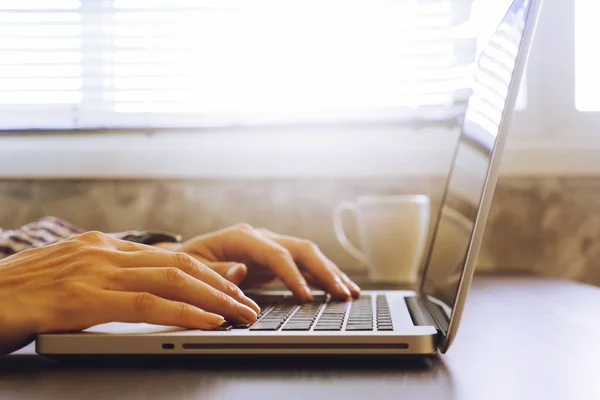 Primer plano de las manos masculinas usando el ordenador portátil en el escritorio, tonificado con luz solar . — Foto de Stock