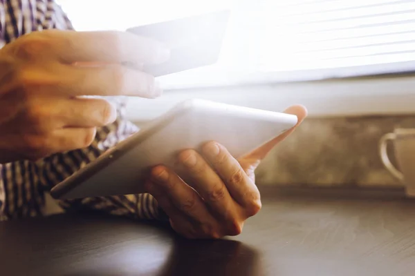 Primer plano de las manos masculinas utilizando la tableta y la celebración de la tarjeta de crédito en el escritorio, enfoque suave, tonificado con luz solar . — Foto de Stock