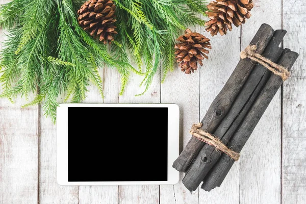 Vista superior del abeto con conos de pino, leña y tableta sobre mesa de madera, fondo de decoración navideña — Foto de Stock