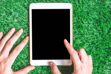Eller erkek yeşil çim zemin üzerine boş dijital tablet kullanma.
