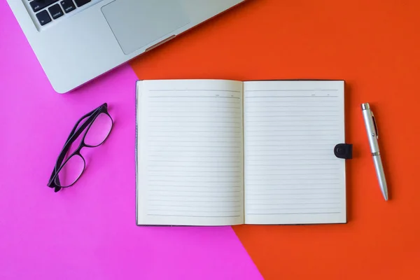 Boş defter kalem, gözlük ve renkli arka plan üstünde laptop ile.