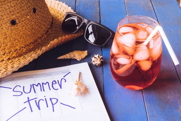 Hat with sunglasses, red cocktail, calendar and seashells on wooden table. Summer holiday concept — Stock Photo, Image