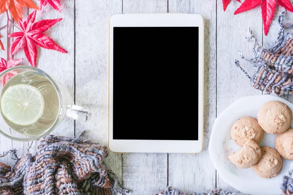 Tablet, cup of tea with lemon, cookie, scarf and maple leaves on wooden table. — Stock Photo, Image