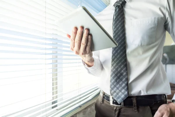 Close up of businessman using tablet device while standing at a window in an office