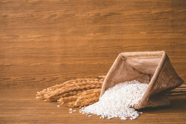 Close up of raw rice in burlap sack on wooden table. — Stock Photo, Image