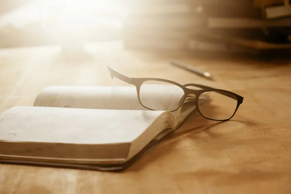 Close up of open notebook with eyeglasses on wooden desk, Soft focus,  Flare sun light,Vintage tone. — Stock Photo, Image