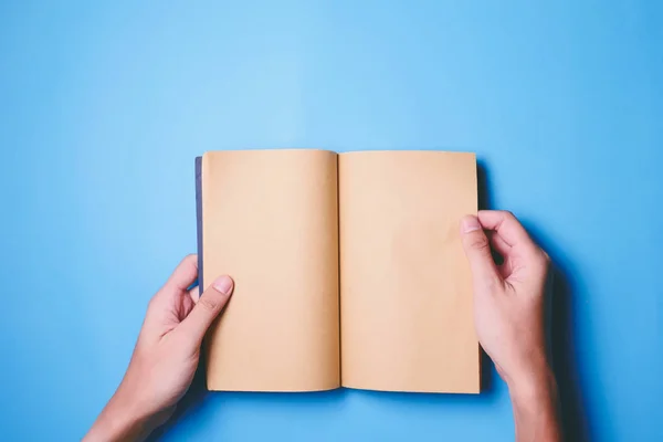 Ansicht von oben der Hände, die ein leeres Buch mit Kopierraum bereit für Text auf blauem Hintergrund halten. — Stockfoto