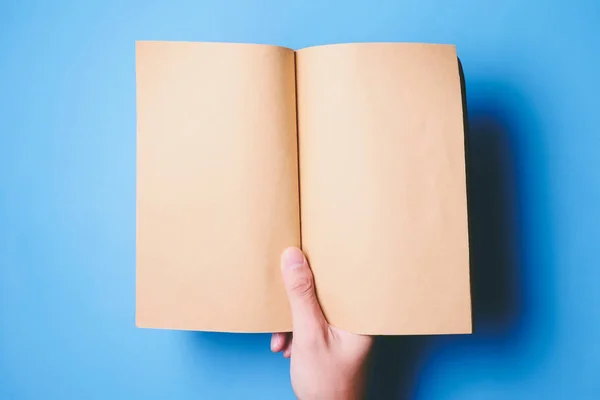 Vista superior de las manos sosteniendo un libro en blanco listo con espacio de copia listo para el texto sobre fondo azul . — Foto de Stock