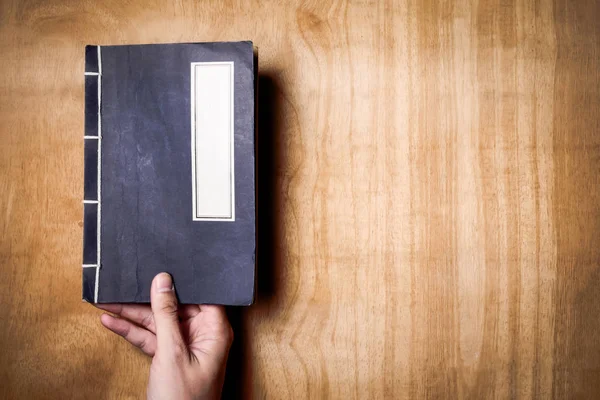 Vista superior de las manos sosteniendo un libro sobre fondo de madera. Espacio libre para texto — Foto de Stock