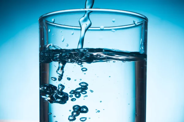 Gießen von Wasser in Glas auf blauem Hintergrund. — Stockfoto