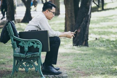 Asya iş adamı işten sonra parkta bankta zor oturmuş bir cep telefonu kullanarak.