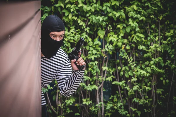 Robber hiding behind the wall, looking at victims and waiting to come nearest for stealing the valuables.