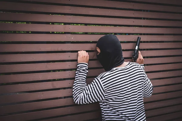 Robber hiding behind the wall, looking at victims and waiting to come nearest for stealing the valuables.