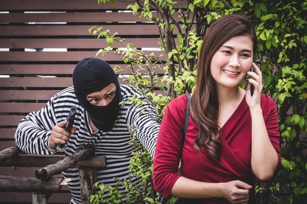 Ladrón está sosteniendo un arma y mirando a la mujer asiática, que está caminando sola, y esperando para robar su bolso . —  Fotos de Stock