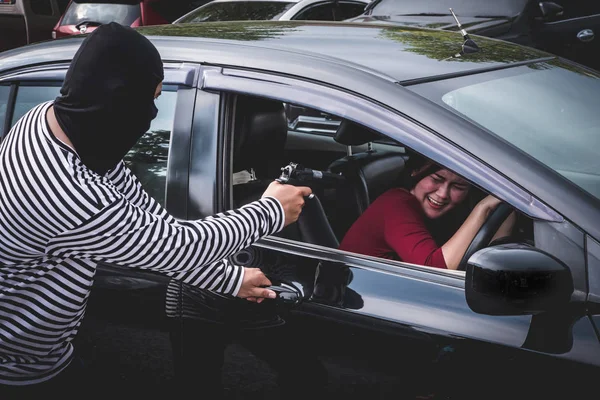 Грабіжник вказує на пістолет, щоб налякати молоду жінку і спробувати пограбувати її машину . — стокове фото