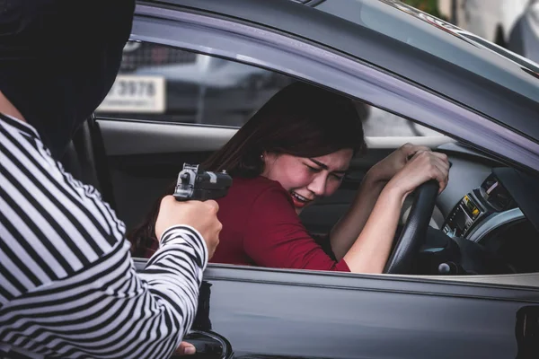 Rabuś wskazując broń do przestraszyć młoda kobieta i próbują obrabować jej samochód. — Zdjęcie stockowe