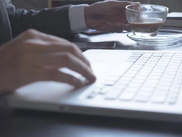 Close up of Businessman drinking coffee and using a laptop on the office desk. — Stock Photo, Image