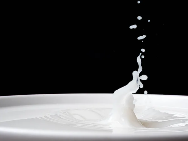 Spritzer Milch aus einer Tasse auf schwarzem Hintergrund. — Stockfoto