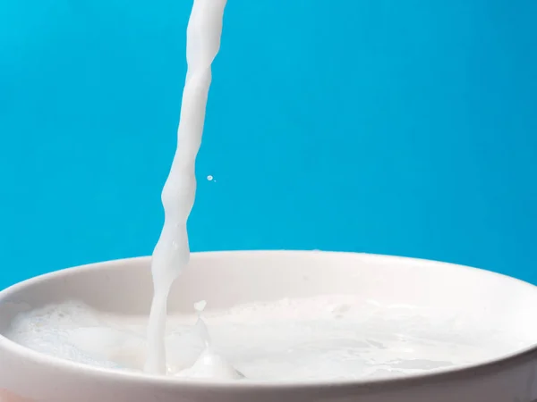 Splash van melk uit een beker op blauwe achtergrond. — Stockfoto