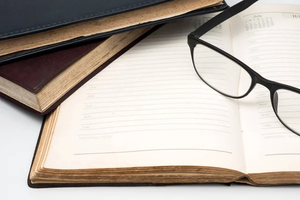 A stack of old books with notebook and eyeglasses on a white background. — Stock Photo, Image