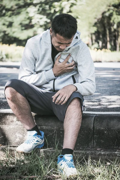 Um jovem asiático tem uma dor de coração enquanto se exercita em um parque . — Fotografia de Stock