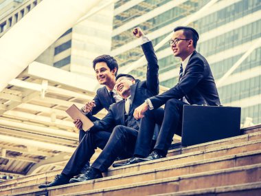 Neşeli grup genç iş adam merdivenlerde ofis binası önünde otururken yeni proje başarıdan sonra harekete geçirilen silah tutmak. Vintage sesi