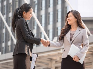 Ofis binası önünde duran ise el sıkışan iki Asya iş kadınları.