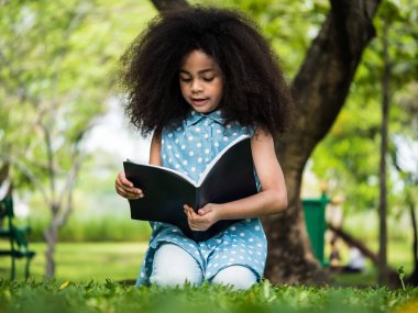 Güzel kız bir parkta yeşil çimenlerin üzerinde otururken bir kitap okuma