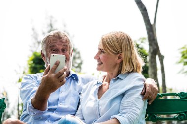 Yaşlı çift parkta akıllı telefonlarıyla selfie çekiyor.