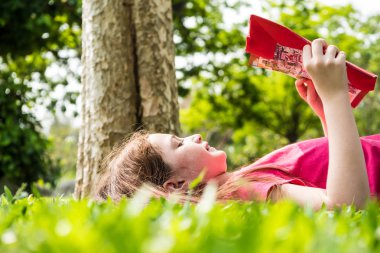 Güzel kız bir parkta yeşil çimenlerin üzerinde bir kitap okuma