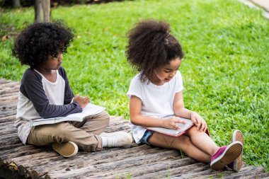 Küçük oğlan ve kız okuma kitabı yerde bir parkta otururken.