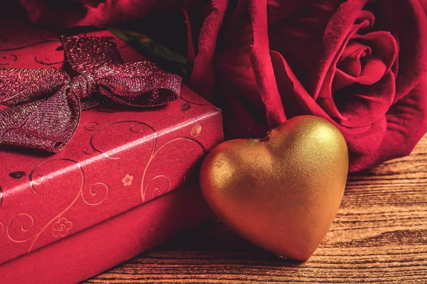 Gold heart with gift box and red rose on wooden background. Concept of Valentine Day.