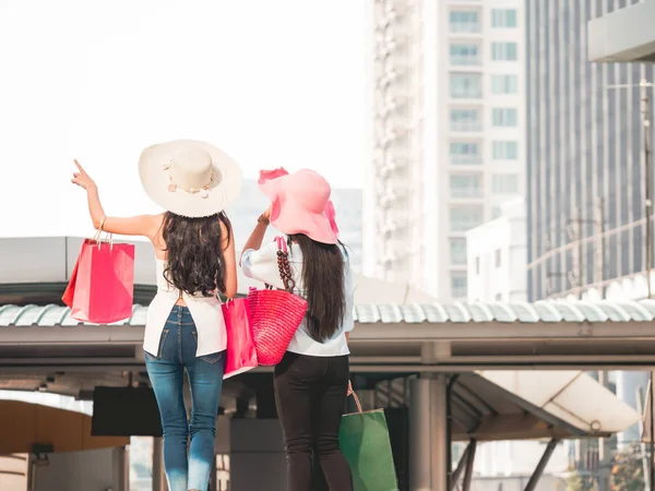 Vista posterior de las mujeres jóvenes con bolsas de compras disfrutando de las compras, chicas asiáticas se están divirtiendo con sus compras en la ciudad. Concepto de consumo y estilo de vida —  Fotos de Stock