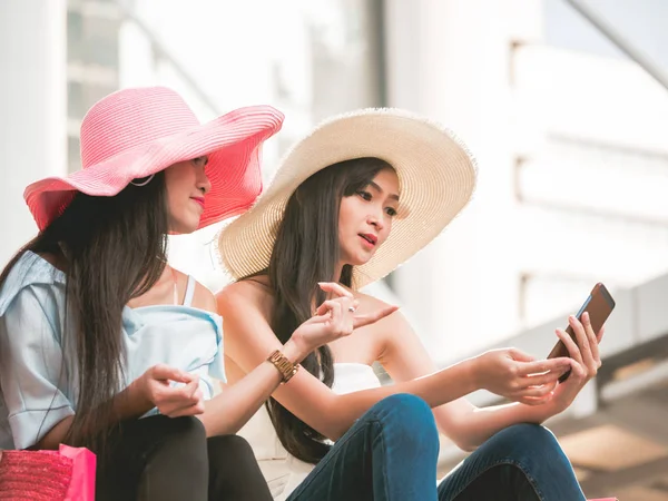 두 아름 다운 젊은 여성이 계단에 앉아서 쇼핑을 즐긴 후 스마트 휴대 전화를 사용 하 여 — 스톡 사진