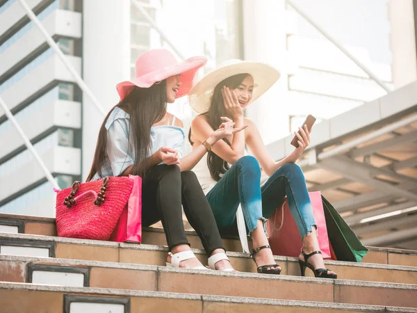 Dos hermosas mujeres jóvenes sentadas en las escaleras y utilizando el teléfono inteligente después de disfrutar en las compras — Foto de Stock