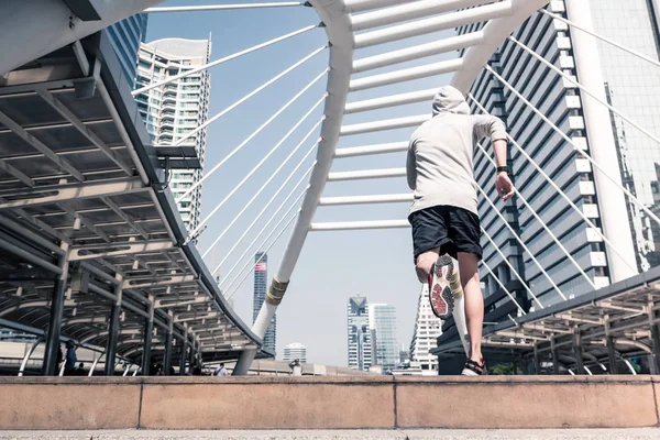 Arkadan görünüş atletik gencin şehir köprüsü üzerinde Bangkok kentsel sahne arka plan ile sabah koşan sportif adam koşu