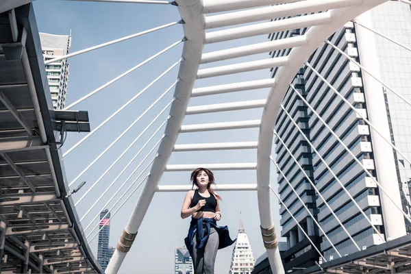 Young athletic woman jogging on city bridge, Sporty woman running at morning with Bangkok urban scene background