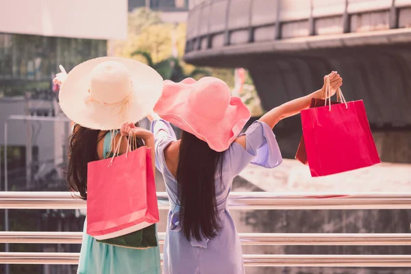 Vista posterior de las mujeres jóvenes con bolsas de compras disfrutando en las compras, Dos chicas se están divirtiendo con sus compras en la ciudad. Concepto de consumo y estilo de vida —  Fotos de Stock