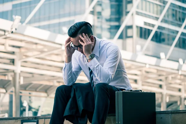 Frustrierter asiatischer junger Geschäftsmann sitzt vor dem Bürogebäude. — Stockfoto