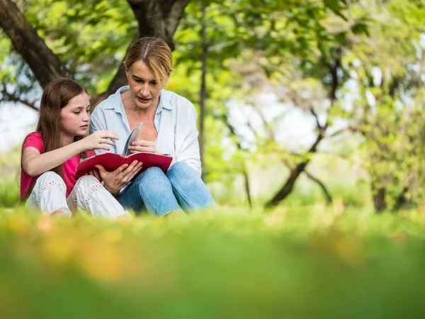 Mãe e filha lendo um livro juntas em um parque. Conceito de família, estilo de vida e educação — Fotografia de Stock