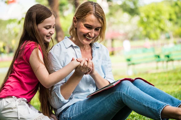 Mãe e filha lendo um livro juntas em um parque. Conceito de família, estilo de vida e educação — Fotografia de Stock