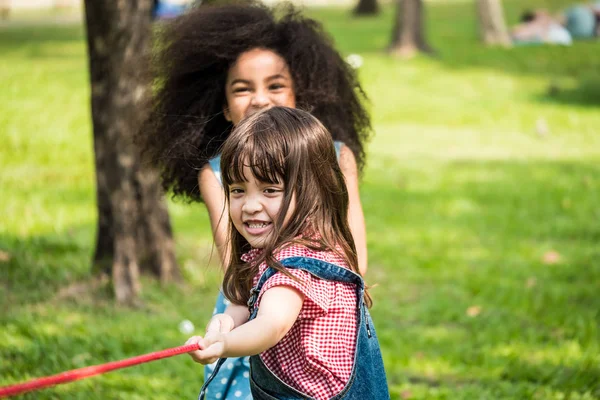 Egy kicsi lány játék kötélhúzás a barátaival, parkban — Stock Fotó