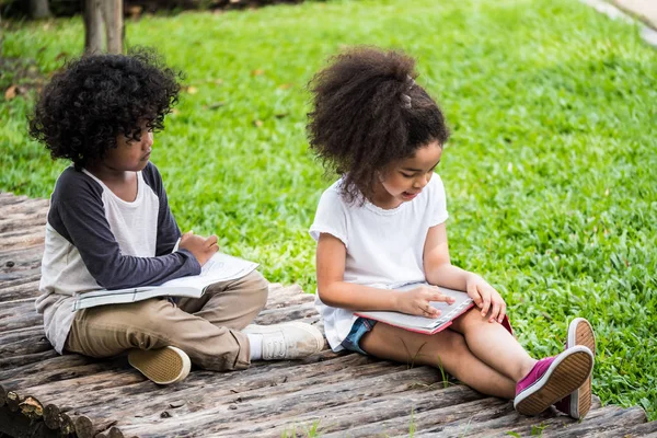 Kisfiú és a lány olvasókönyv rövid idő ülő a földön egy parkban. — Stock Fotó